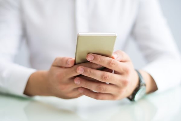 Close-up of manager checking message on phone. Unrecognizable man sitting at table and watching online video on smartphone. Gadget concept